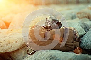 Old vintage film medium format camera lies on the stones against the backdrop of a canvas vintage backpack