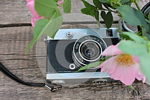 Old vintage film photo camera and flowers on wooden background with copy space.