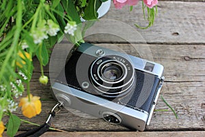 Old vintage film photo camera and flowers on wooden background with copy space.