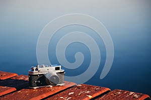 Old vintage film photo camera lying on wooden berth, dark blue water background. Copy space