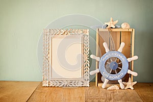 Old vintage frame with naurical wheel on wooden table. vintage filtered image