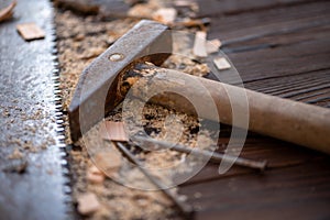 Old vintage hammer, wood saw, nails and sawdust on a wooden background, close-up, selective focus