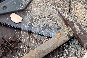 Old vintage hammer, wood saw, nails and sawdust on a wooden background, close-up, selective focus