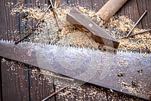 Old vintage hammer, wood saw, nails and sawdust on a wooden background, close-up, selective focus