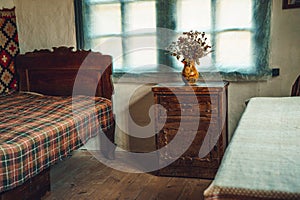 Old vintage historic room with wooden bed, bedside table and vase of flowers