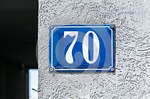 Old vintage house address metal number 70 seventy on the plaster facade of abandoned home exterior wall on the street side photo