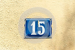 Old vintage house address metal plate number 15 fifteen on the plaster facade of abandoned home exterior wall on the street side