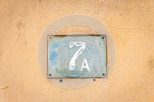 Old vintage house address metal plate number 7 A seven on the plaster facade of abandoned home exterior wall on the street side