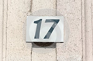 Old vintage house address metal plate number 17 seventeen on the plaster facade of abandoned home exterior wall on the street side