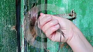 Old vintage iron lock on the door with green paint peeled. Female hand opens and closes lock