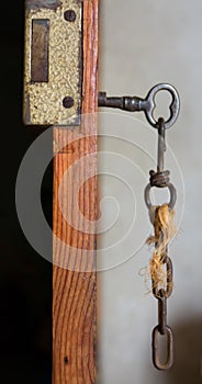 old or vintage key made by metallic iron inside a lock of a wooden door which is opened. The old key and the lock are completely