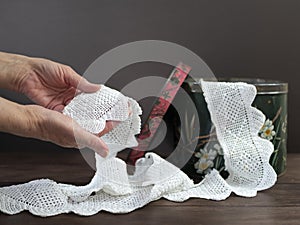 Old vintage lace ribbon in woman hands. Still life with white lace and old box