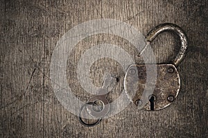 Old vintage lock with key. Ancient rusty barn lock with key on wooden textured background.