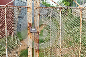 Old vintage lock is on the rusty iron gate with ragged rope net