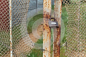 Old vintage lock is on the rusty iron gate with ragged rope net