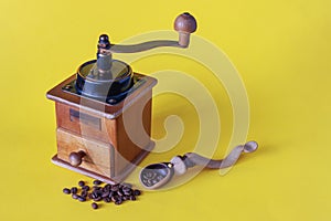 Old Vintage Manual Coffee Grinder with Wooden Spoon and Coffee Beans on Yellow Background