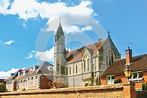 Old vintage medieval beautiful stone british church with tile roof, old traditional houses and a garden behind the brick wall in