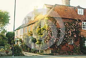 Old vintage medieval beautiful stone british house with tile roof and bright windows, a flowering rose garden near the asphalt