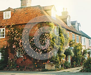 Old vintage medieval beautiful stone british house with tile roof and bright windows, a flowering rose garden near the asphalt