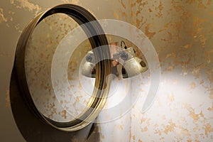 Old vintage mirror and wall lamp in gray on a wooden base, on a silver-gold wall background close up photo.