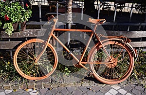 Old Vintage Orange Bicycle supported by a wooden fence