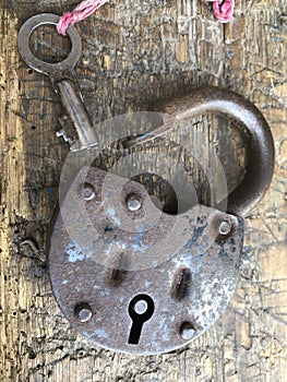 Old vintage padlock. The lock of the lock is open. Nearby is the key to the padlock. Against the background of an old wooden shed.