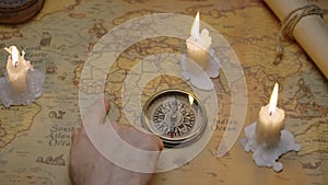 Old vintage retro compass on ancient map. Composition illuminated by candles. Male hand indicates the route.