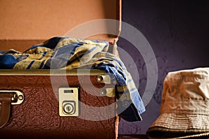 Old vintage, retro open suitcase with hats and checkered shirt on dark background. Travel concept