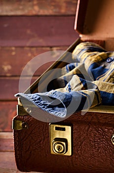 Old vintage, retro open suitcase with man`s checkered shirt on dark background. Travel concept. Vertical