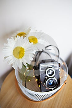 Old vintage rustic camera with a bouquet of daisy flowers on a wooden board
