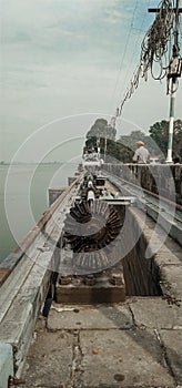 Old vintage rusty machinery and gears on side of a road over a large water body