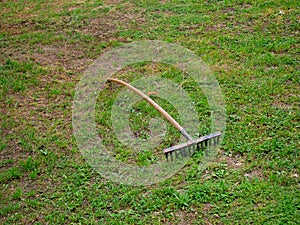 Old vintage rusty metal rake with a wooden handle on the ground with green grass