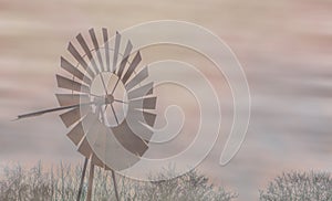 A old vintage rusty windmill in the mist, classical landscape, agricultural or western background