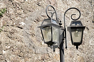 Old vintage street lamp, glass lantern and black iron decorations on light brown stone wall background on sunny