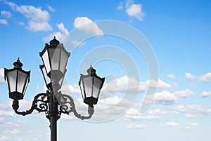 Old vintage street lamp post or lantern with light bulbs against a beautiful blue sky with white clouds background