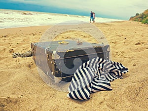 Old vintage suitcase for travel and family vacations lies on the beach. Man and woman in love Sea shore ocean. Photo in a trendy