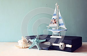 Old Vintage sutcase with toy boat' starfish and seashell on wooden board. travel and voyage concept. retro filtered image.