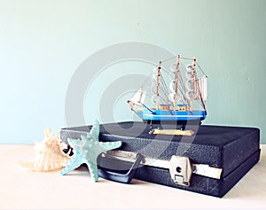 Old Vintage sutcase with toy boat' starfish and seashell on wooden board. travel and voyage concept. retro filtered image