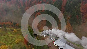 Old vintage train locomotive moving through the breathtaking forest valley in mountains, autumn colors, drone shot