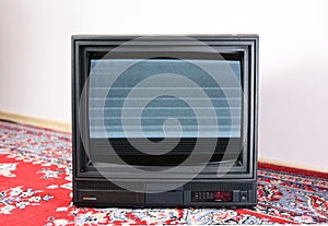 An old vintage TV set from the 1980s, 1990s, 2000s with noise and interference on the screen stands on a bright Soviet carpet on t