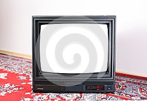 An old vintage TV with a white screen from the 1980s, 1990s, 2000s stands on a bright Soviet carpet on the floor.