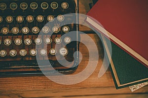 Old and vintage type writer machine and piles of books on wooden table - in vintage tone