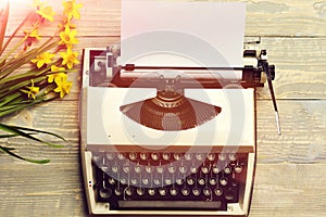 Old vintage typewriter with paper and spring blossoming narcissus flowers