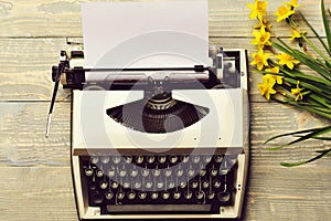 Old vintage typewriter with paper and spring blossoming narcissus flowers