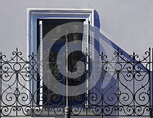 Old vintage window with ornate fence, gate wrought iron bars. Wrought Iron Gate. Facade of a house with wooden shutters. sunny day