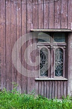 Old vintage window on a wooden house. brown background. Green grass at the bottom.