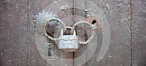 Old vintage wooden door locked with rusty padlock on metal double handle. Close up, banner