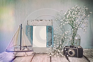 Old vintage wooden frame, white flowers, photo camera and sailing boat on wooden table. vintage filtered image