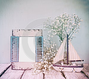 Old vintage wooden frame, white flowers and sailing boat on wooden table. vintage filtered image. nautical lifestyle concept