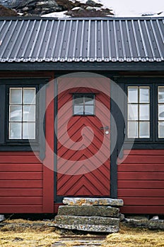 An old vintage wooden front door with window on a red country house. Facade exterior. Retro Scandinavian countryside